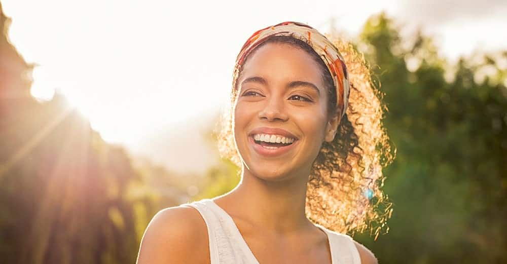 A woman with healthy, white teeth smiles broadly on a sunny day.